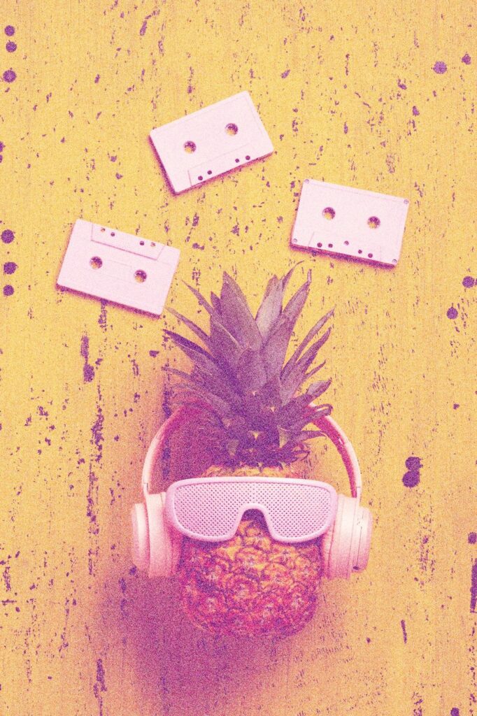 Un ananas avec lunettes de soleil et casque audio, entouré de cassettes